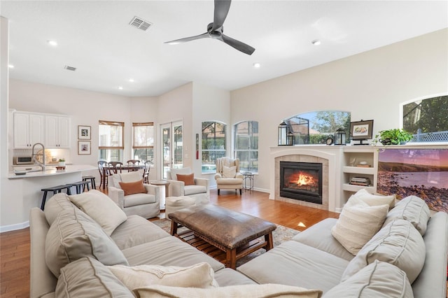 living room featuring ceiling fan, a tile fireplace, and light hardwood / wood-style floors