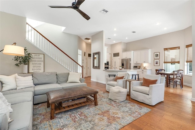 living room featuring light hardwood / wood-style floors, a high ceiling, and ceiling fan