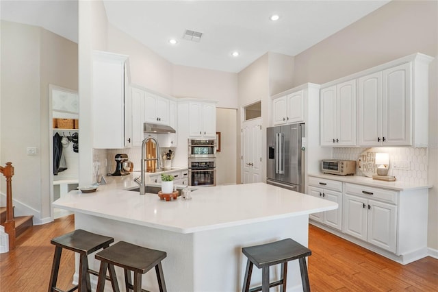 kitchen featuring light hardwood / wood-style floors, kitchen peninsula, a breakfast bar area, stainless steel appliances, and white cabinets