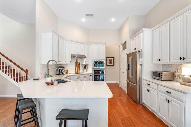 kitchen featuring kitchen peninsula, appliances with stainless steel finishes, white cabinets, a breakfast bar, and sink