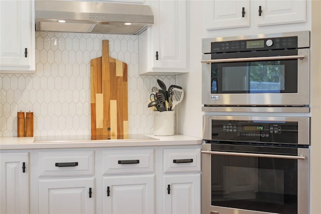 kitchen featuring ventilation hood, white cabinetry, double oven, and backsplash