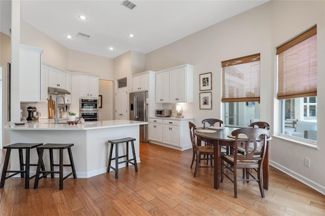 kitchen featuring white cabinetry, kitchen peninsula, appliances with stainless steel finishes, decorative backsplash, and a kitchen breakfast bar