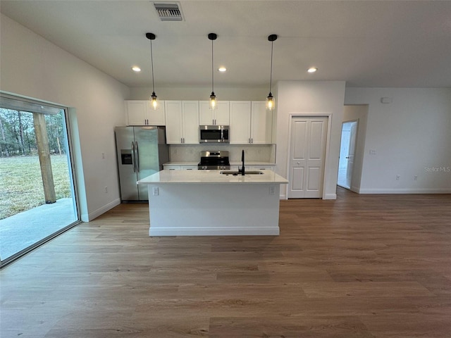 kitchen with appliances with stainless steel finishes, pendant lighting, sink, white cabinets, and a center island with sink