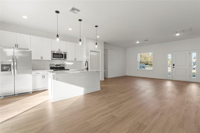 kitchen with pendant lighting, an island with sink, white cabinets, stainless steel appliances, and light wood-type flooring