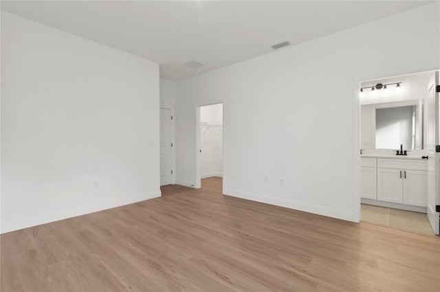 unfurnished bedroom with connected bathroom, a spacious closet, sink, and light hardwood / wood-style flooring