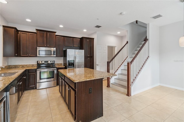 kitchen with light stone counters, appliances with stainless steel finishes, light tile patterned flooring, and a kitchen island