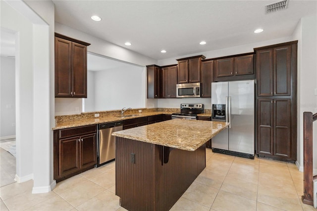 kitchen featuring light tile patterned floors, sink, appliances with stainless steel finishes, a kitchen island, and a kitchen bar