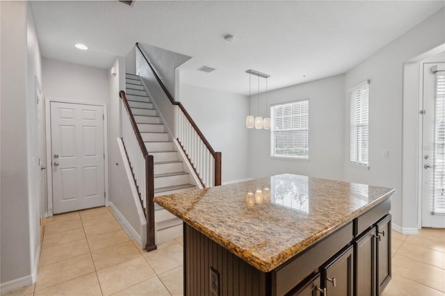 kitchen featuring pendant lighting, a center island, dark brown cabinetry, light stone countertops, and light tile patterned flooring