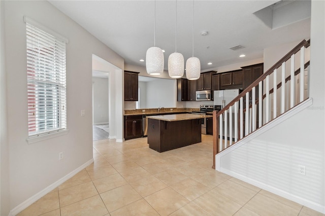 kitchen with a breakfast bar, appliances with stainless steel finishes, a center island, light tile patterned flooring, and decorative light fixtures