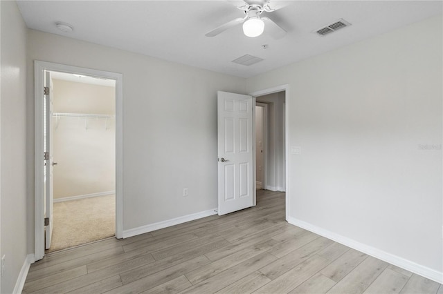 unfurnished bedroom with a spacious closet, light hardwood / wood-style floors, a closet, and ceiling fan