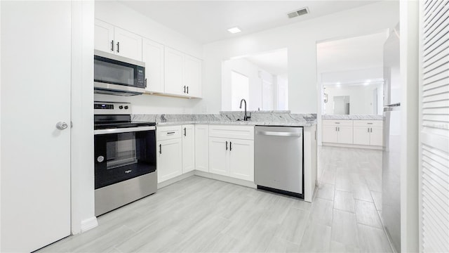 kitchen featuring sink, white cabinets, light stone countertops, and appliances with stainless steel finishes