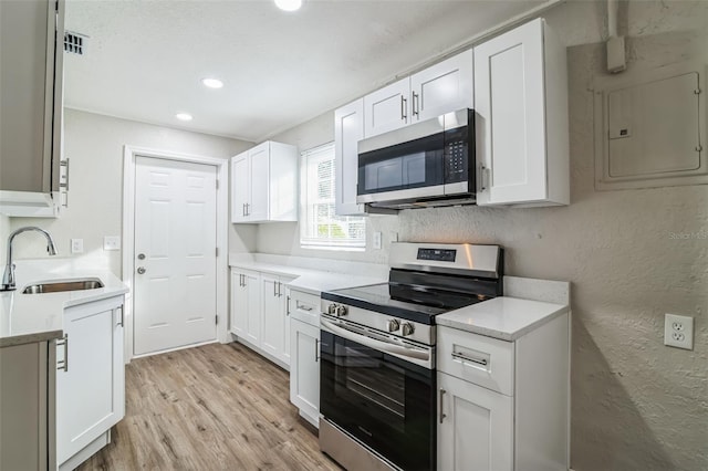 kitchen featuring white cabinetry, stainless steel appliances, light wood-type flooring, electric panel, and sink