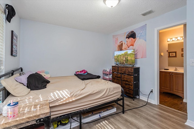 bedroom featuring ensuite bathroom, sink, a textured ceiling, and light hardwood / wood-style floors