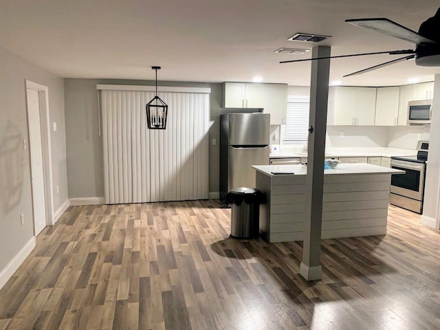 kitchen with white cabinets, a kitchen island, wood-type flooring, stainless steel appliances, and hanging light fixtures