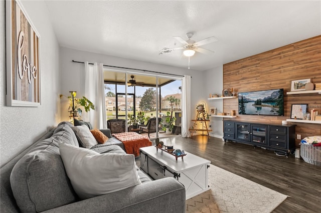 living room with a textured ceiling, dark hardwood / wood-style floors, wood walls, and ceiling fan