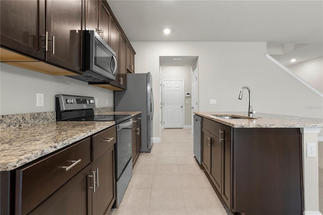 kitchen with sink, light stone counters, dark brown cabinets, a center island with sink, and stainless steel appliances