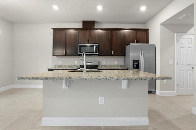 kitchen with light stone countertops, an island with sink, appliances with stainless steel finishes, and sink