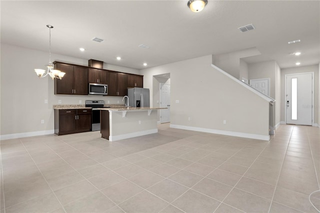 kitchen featuring hanging light fixtures, light tile patterned floors, stainless steel appliances, and an island with sink