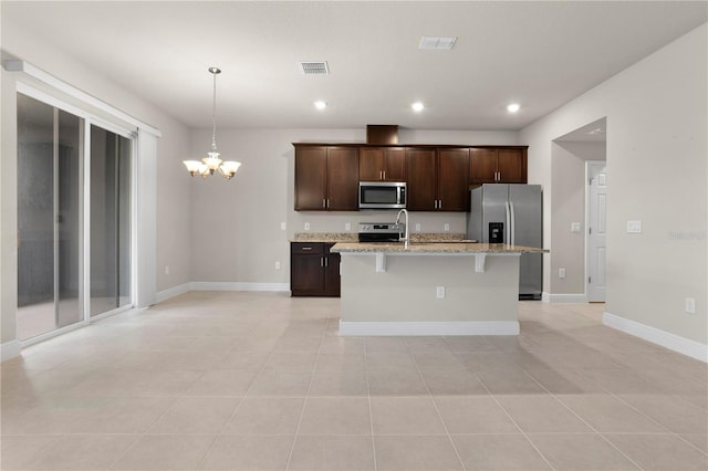 kitchen with stainless steel appliances, light stone counters, a notable chandelier, dark brown cabinetry, and an island with sink