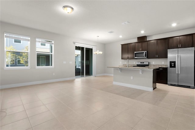 kitchen with appliances with stainless steel finishes, an island with sink, a kitchen bar, hanging light fixtures, and dark brown cabinetry