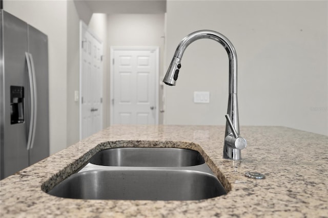 kitchen featuring sink, light stone countertops, and stainless steel refrigerator with ice dispenser