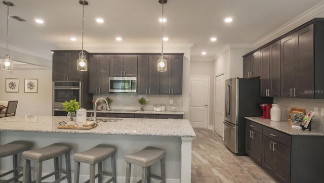 kitchen with light stone counters, sink, hanging light fixtures, and appliances with stainless steel finishes