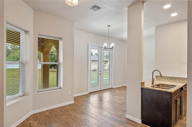 kitchen featuring decorative light fixtures, sink, a chandelier, light stone counters, and light hardwood / wood-style flooring