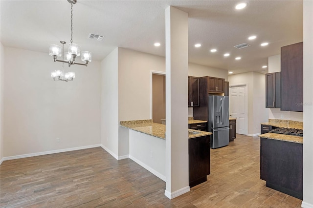 kitchen with decorative light fixtures, dark brown cabinets, light wood-type flooring, stainless steel fridge, and light stone countertops