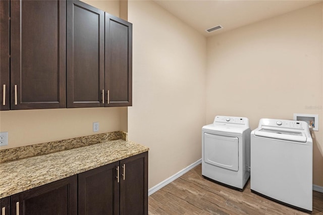 clothes washing area with cabinets, light wood-type flooring, and washer and clothes dryer