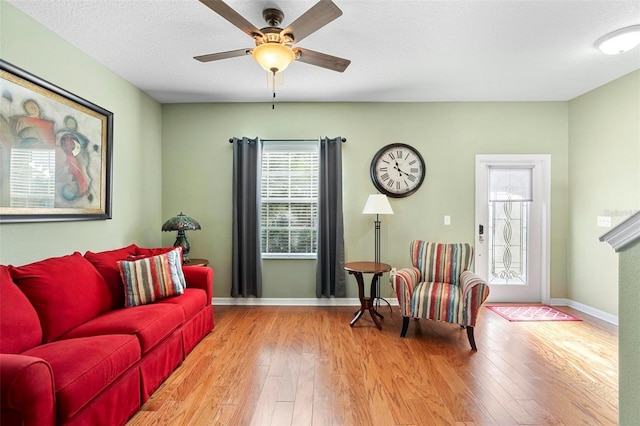 living room featuring light wood-type flooring, ceiling fan, and a textured ceiling