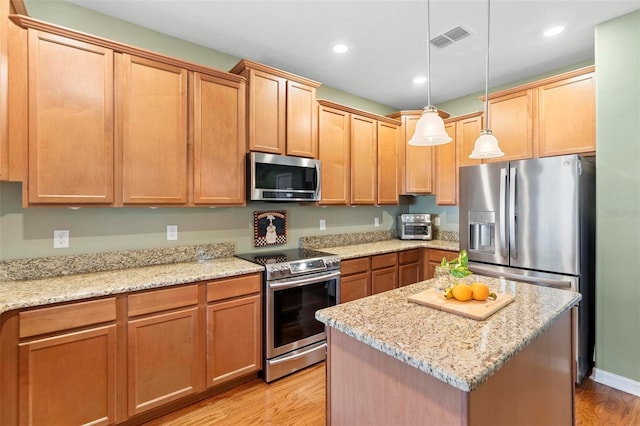 kitchen with a center island, light stone countertops, light hardwood / wood-style flooring, pendant lighting, and stainless steel appliances