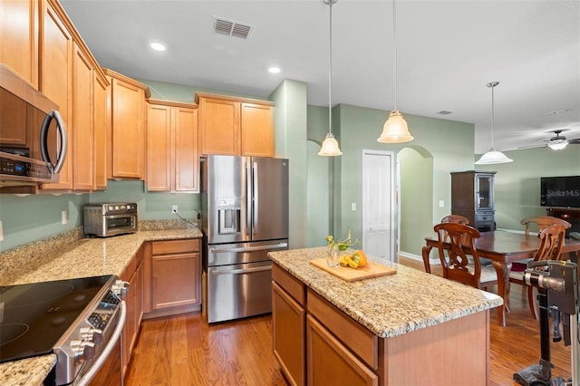 kitchen with a center island, light stone countertops, light hardwood / wood-style floors, hanging light fixtures, and stainless steel appliances