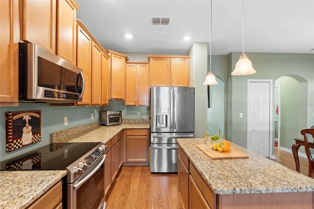 kitchen featuring a center island, appliances with stainless steel finishes, light wood-type flooring, decorative light fixtures, and light stone counters