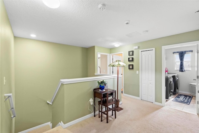 hall featuring washer and dryer, a textured ceiling, and light carpet