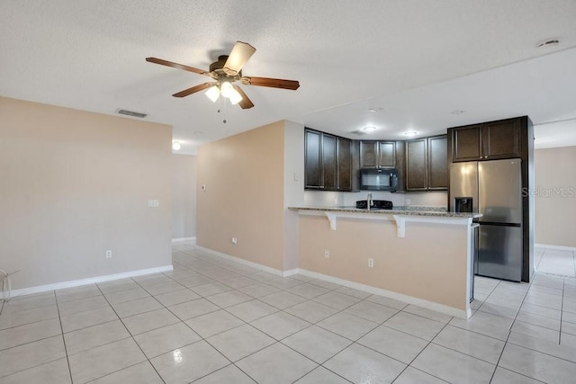 kitchen with a breakfast bar, kitchen peninsula, dark brown cabinetry, light tile patterned floors, and stainless steel fridge