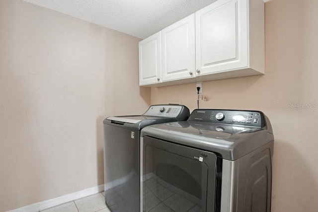 laundry area with washing machine and dryer, cabinets, light tile patterned flooring, and a textured ceiling