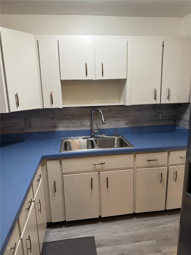 kitchen with dark countertops, light wood-style floors, white cabinets, and a sink