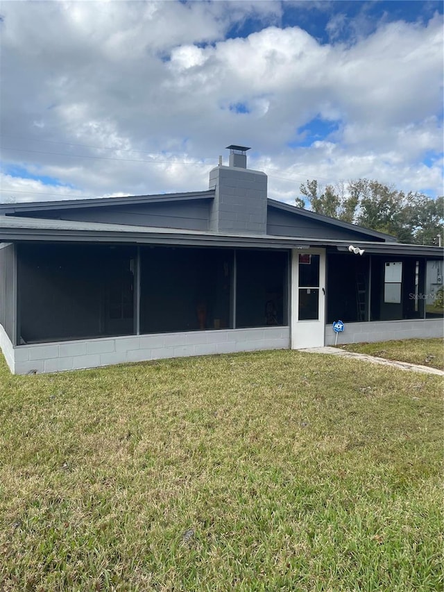 back of house with a sunroom, concrete block siding, and a lawn