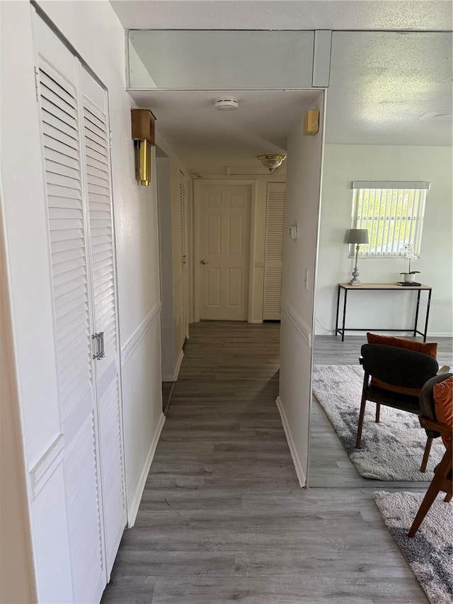 hall with a textured ceiling, wood finished floors, and baseboards