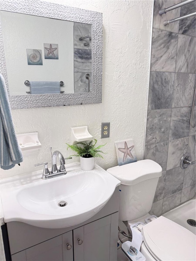 bathroom with toilet, a textured wall, a tile shower, and vanity