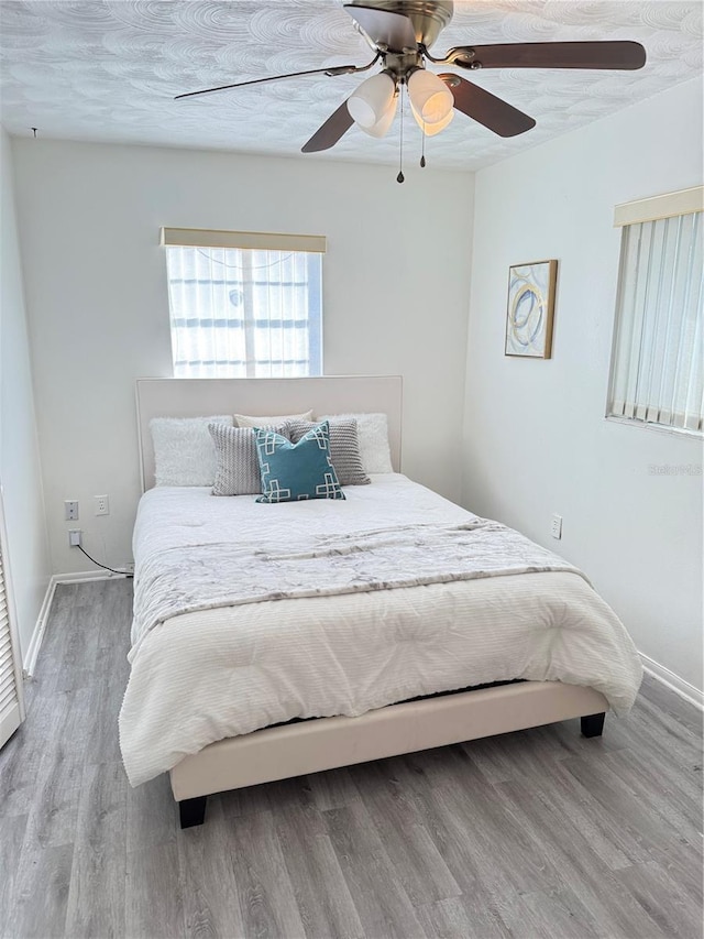 bedroom with ceiling fan, a textured ceiling, baseboards, and wood finished floors