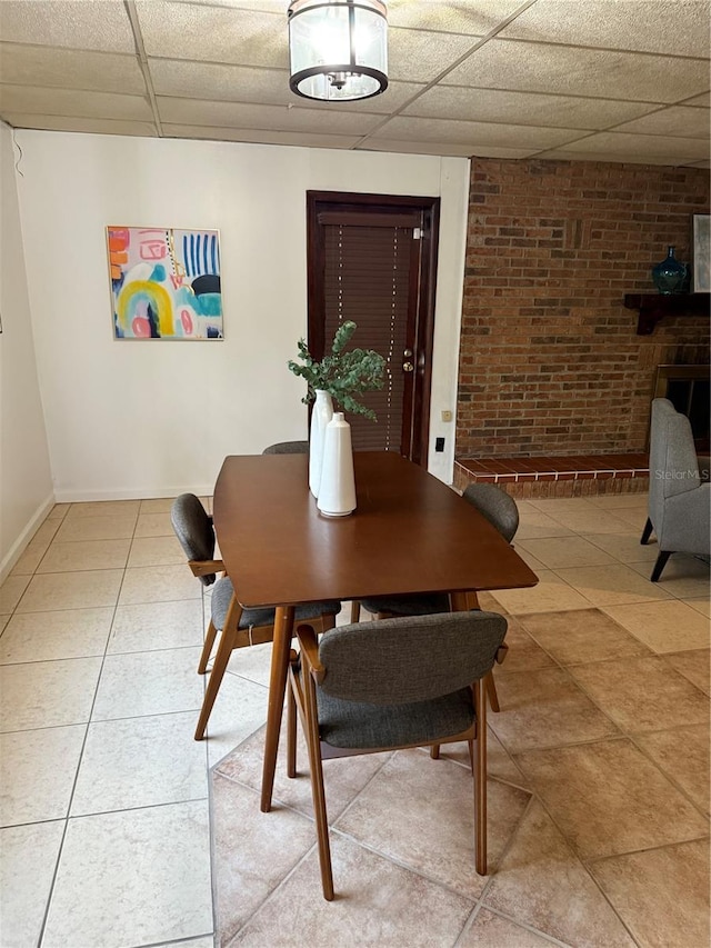 dining room with a paneled ceiling, brick wall, baseboards, and tile patterned floors