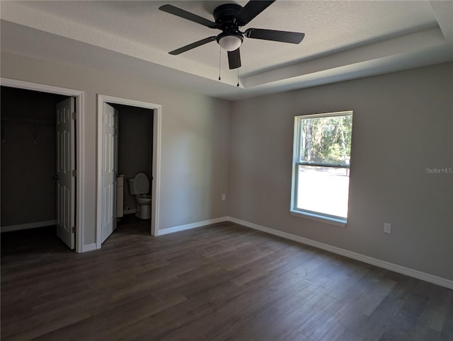 unfurnished bedroom featuring ceiling fan, connected bathroom, a tray ceiling, and a walk in closet