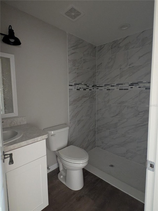 bathroom with toilet, vanity, wood-type flooring, and a tile shower