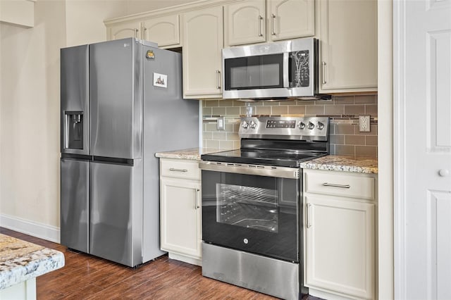 kitchen featuring appliances with stainless steel finishes, decorative backsplash, light stone countertops, dark wood-type flooring, and cream cabinetry