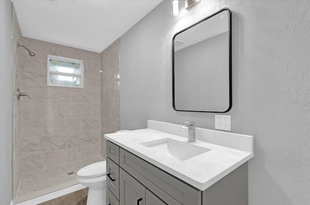 bathroom with toilet, vanity, and a tile shower