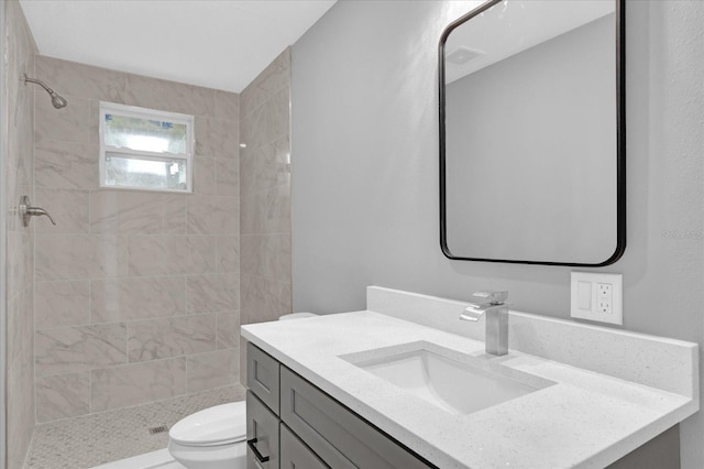 bathroom with toilet, vanity, and tiled shower