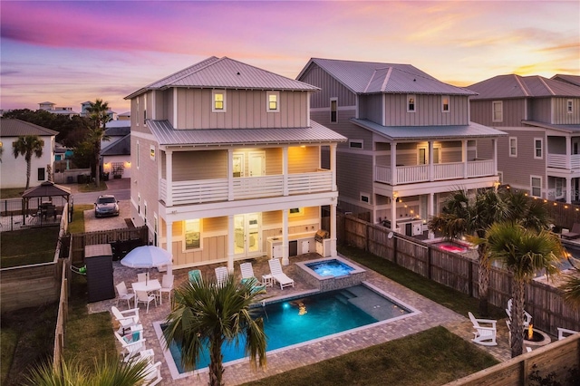 back house at dusk featuring a swimming pool with hot tub, a patio area, and a balcony