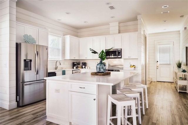 kitchen featuring white cabinetry, a center island, stainless steel appliances, hardwood / wood-style floors, and backsplash