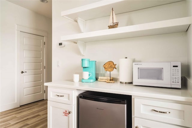 bar with light hardwood / wood-style flooring, stainless steel refrigerator, and white cabinets